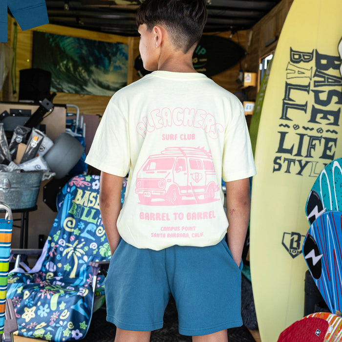 Youth model wearing blue youth shorts with "Bleachers Surf Club" design
