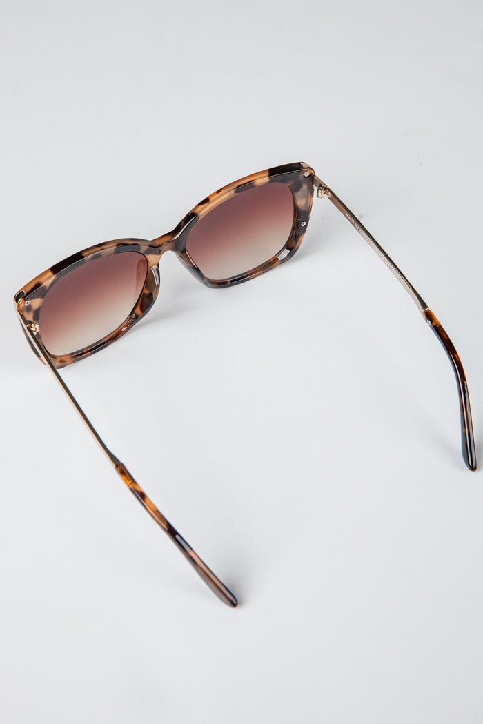 Sunglasses with tortoiseshell frame and brown lenses on a light gray background