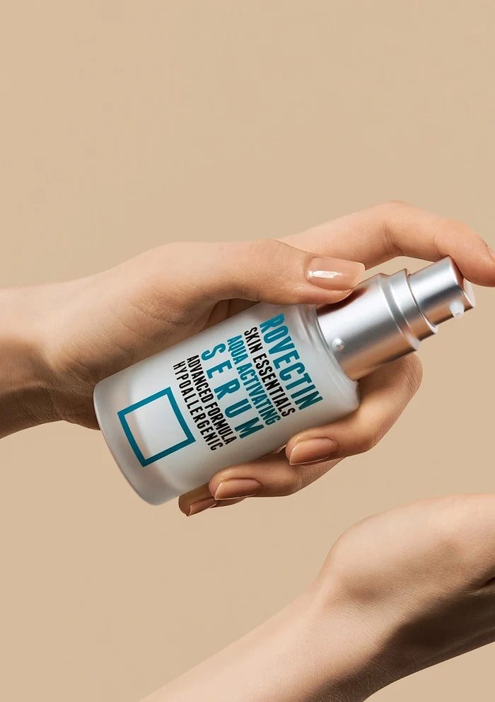 Hand holding a skincare serum bottle against a beige background