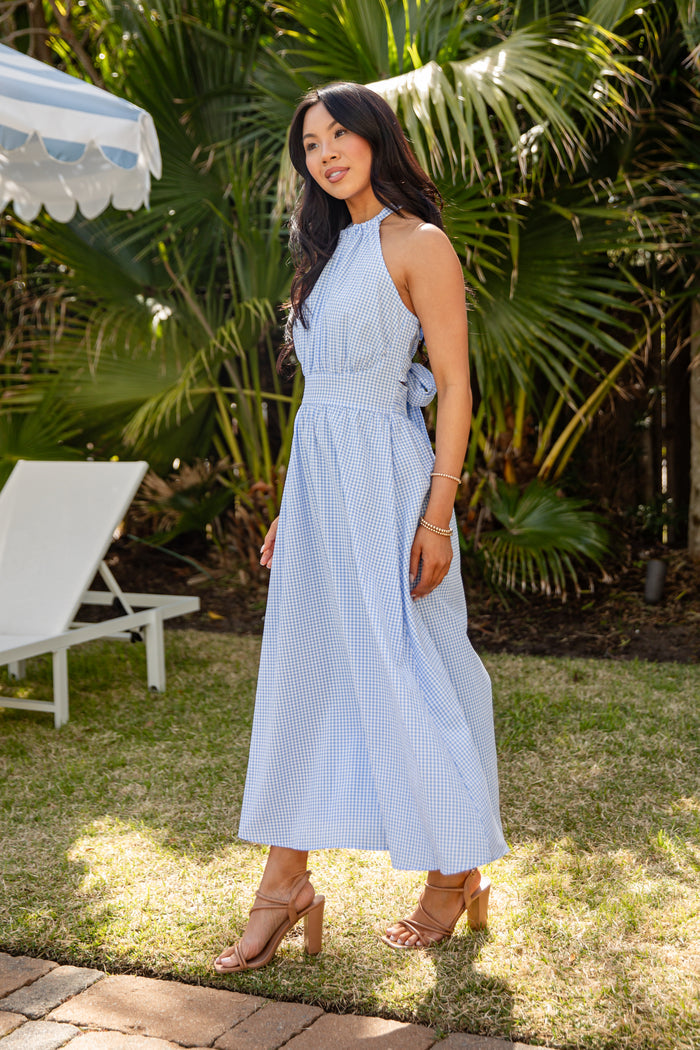Woman in a light blue dress standing outdoors with palm trees in the background