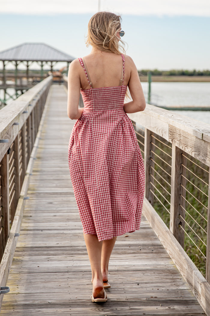 Woman in a red checkered dress walking on a wooden dock by a body of water.