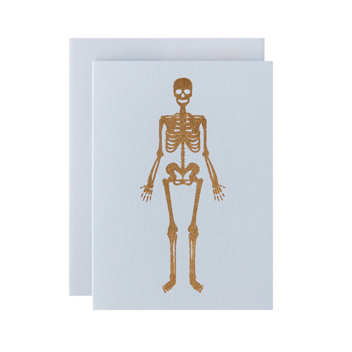 A gold foiled human skeleton on a light grey background, with a matching envelope.