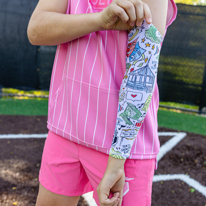 Youth player pulling on the white Jackson Olson x BL101 arm sleeve showing the colorful illustrated print