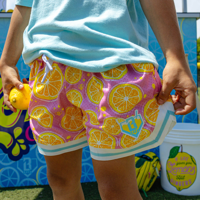 Youth model wearing pink youth shorts with "Lemon Squeeze Court" design