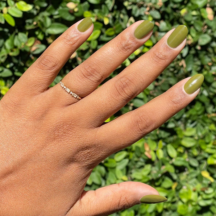 Hand with nails painted in glossy Mossy gel polish displaying smooth quick dry manicure against leafy background