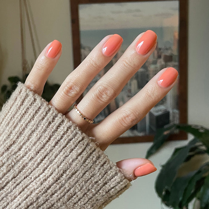 Hand with Peeptoe warm peach quick dry polish on natural nails against cozy indoor background