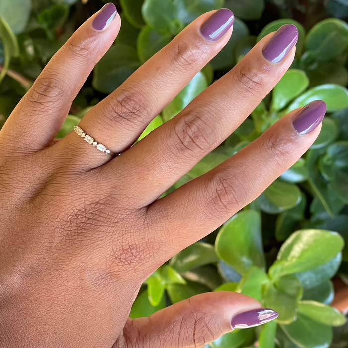 Hand with almond shaped nails in glossy Plum gel polish showing a smooth quick dry manicure over green leafy plants background