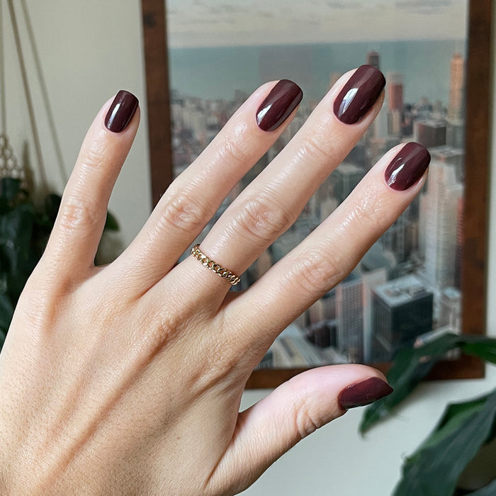 Hand with glossy Spressotini gel polish manicure in deep coffee brown on natural medium-length nails by window background