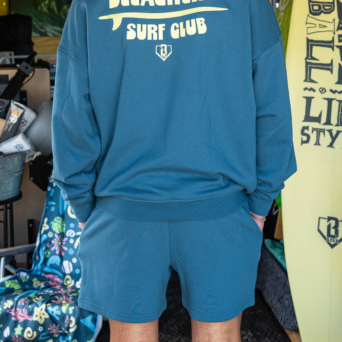 Adult model wearing blue shorts with "Bleachers Surf Club" design