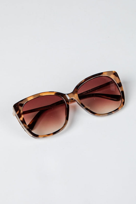 Sunglasses with tortoiseshell frame and brown gradient lenses on a light gray background