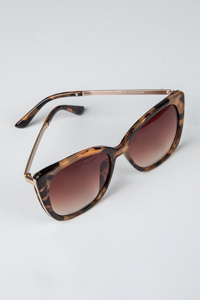Tortoiseshell sunglasses with brown lenses on a light gray background