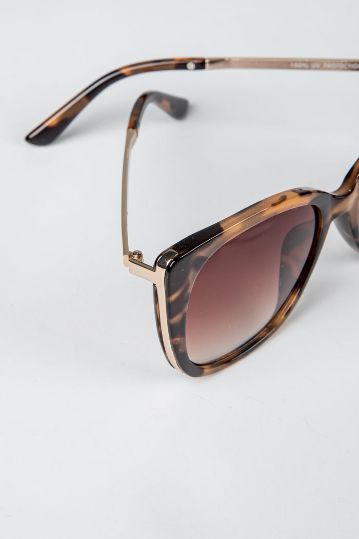 Sunglasses with tortoiseshell frame and brown gradient lenses on a light gray background