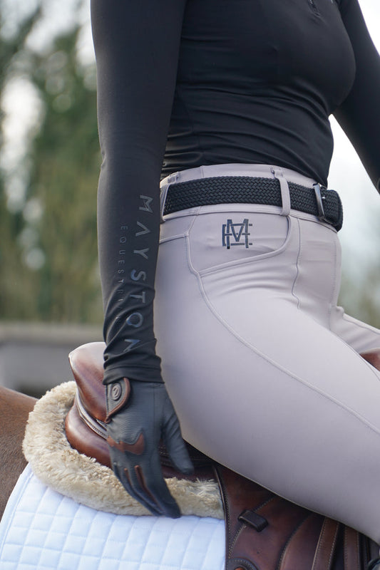 Person wearing equestrian gloves and pants with visible branding, sitting on a horse. Black elastic equestrian belt