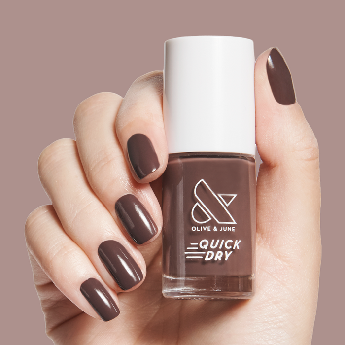 Bunny deep neutral brown quick dry gel polish shown on hand holding bottle against soft mauve background
