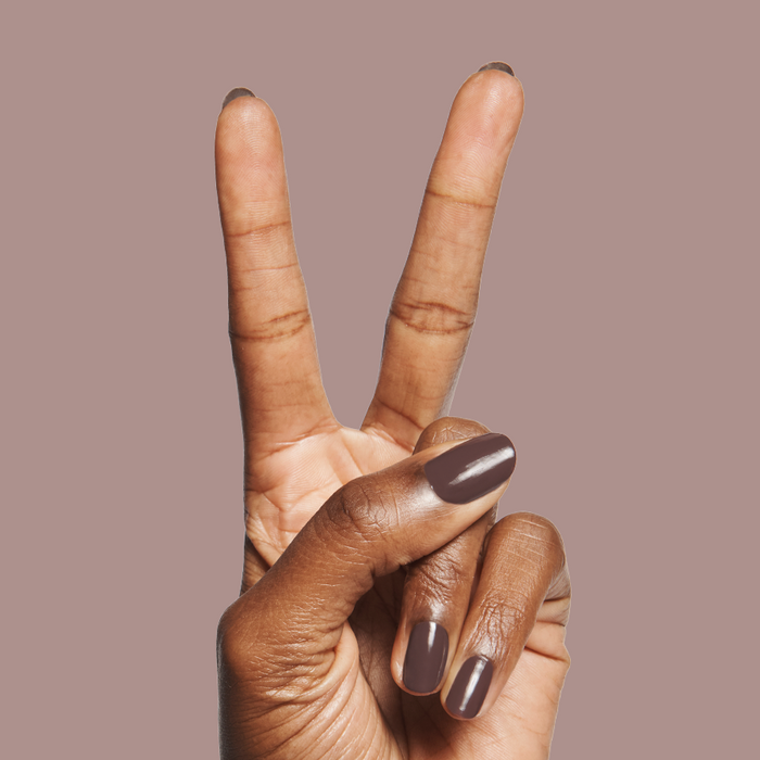 Bunny deep neutral brown quick dry gel polish shown on hand with peace sign against muted mauve background