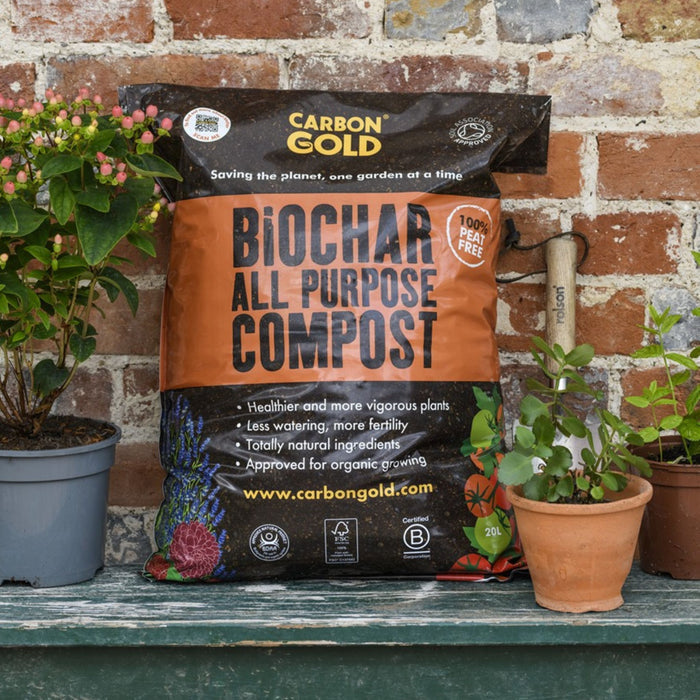 A bag of Carbon Gold Biochar All Purpose Compost placed on a bench with potted plants in the background.