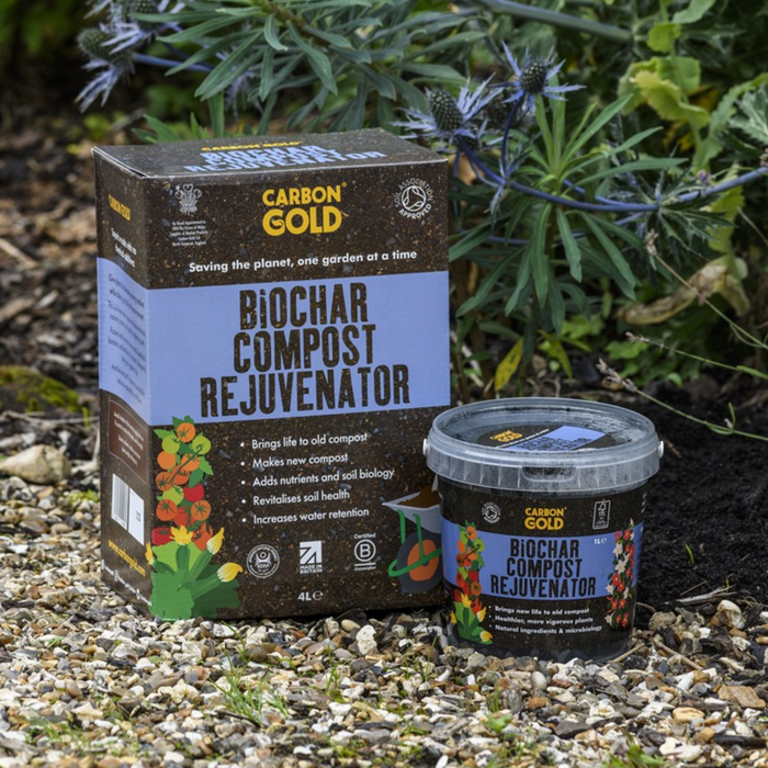 A product image showing a box and a tub of Carbon Gold Biochar Compost Rejuvenator placed on a garden setting with plants in the background.