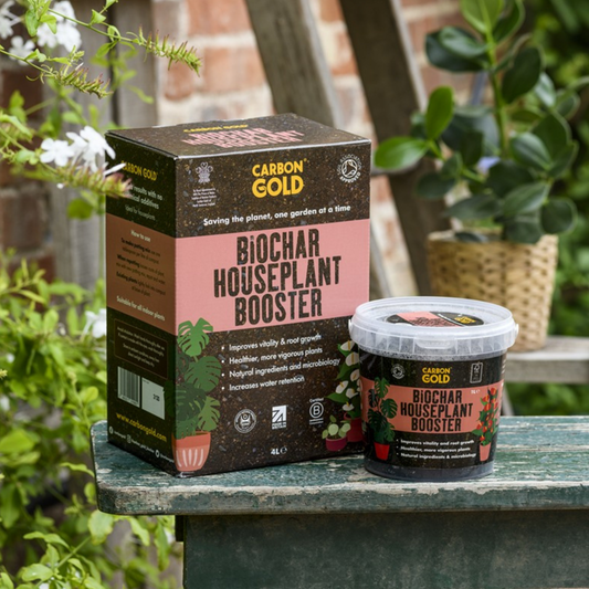 A package and a container of Carbon Gold Biochar Houseplant Booster placed on a wooden surface with plants in the background.