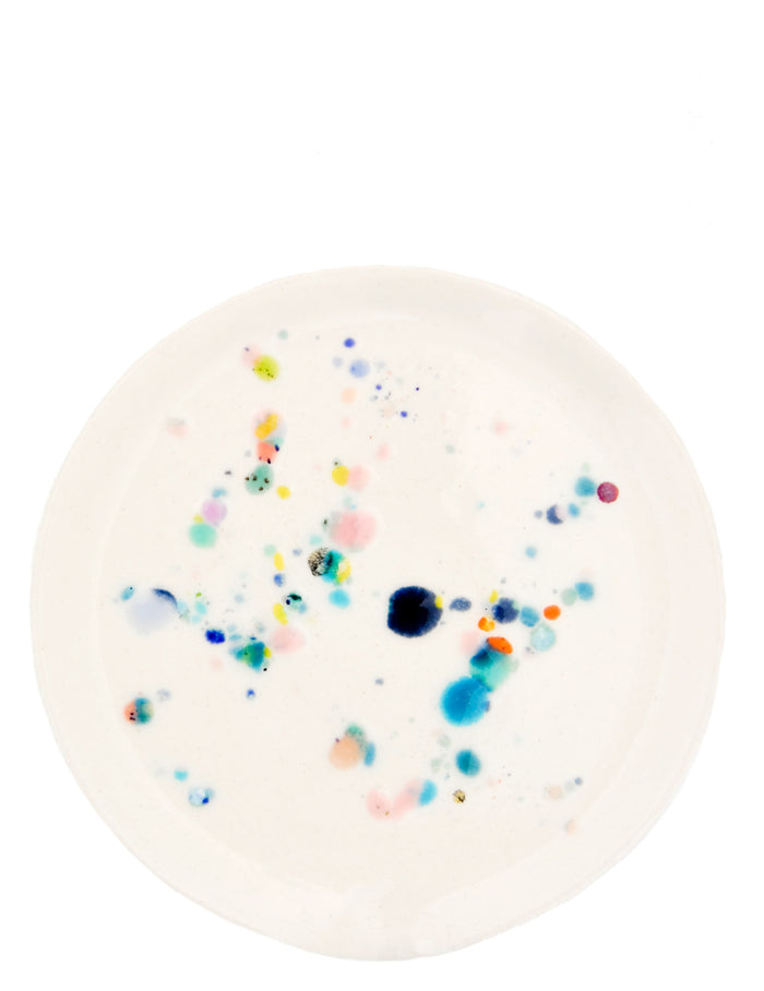 A round ceramic spoon rest with random, colorful glaze drips.