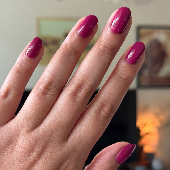 Hand with natural nails painted in Darling quick dry gel polish hot magenta showing glossy smooth manicure at home