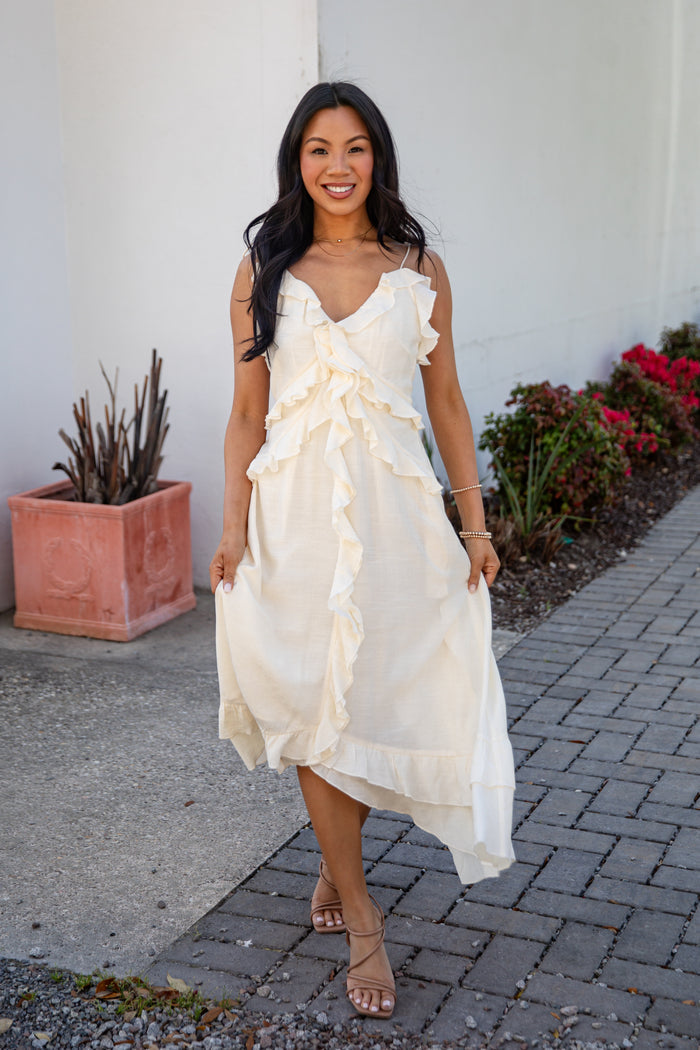 Woman in a white dress standing on a sidewalk with plants in the background