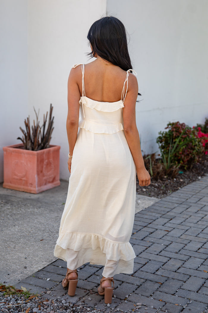 Woman in a white dress walking on a sidewalk with plants and a white wall in the background
