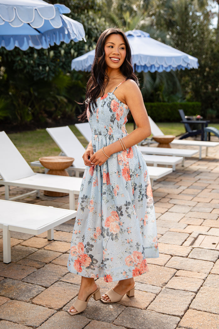 Woman in a floral dress standing in an outdoor setting with lounge chairs and umbrellas.