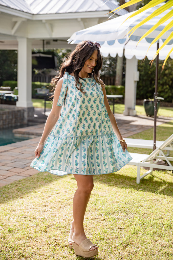 Woman in a light blue dress with a pineapple pattern standing in a garden.