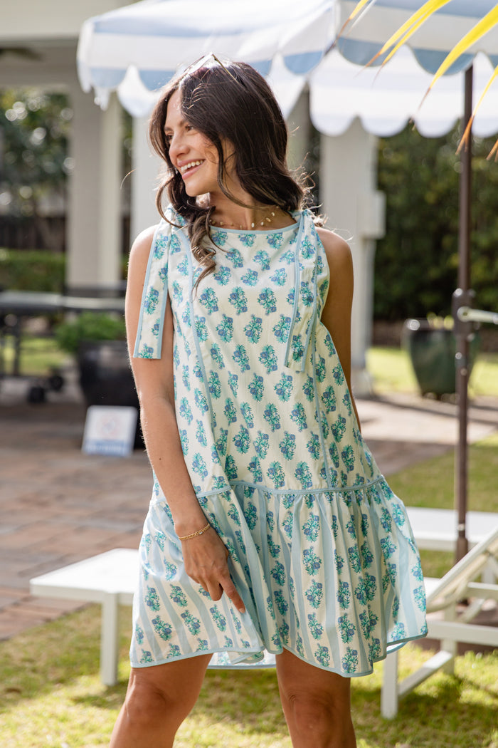 Woman wearing a floral dress standing outdoors under a canopy.