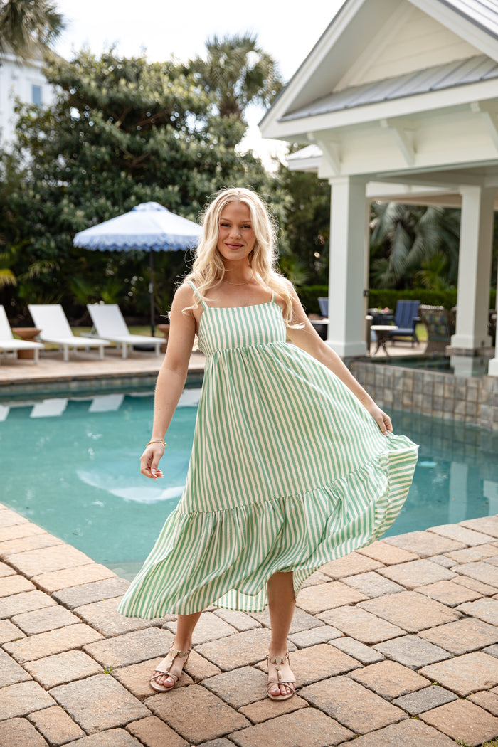 Woman in a green and white striped dress standing by a poolside.