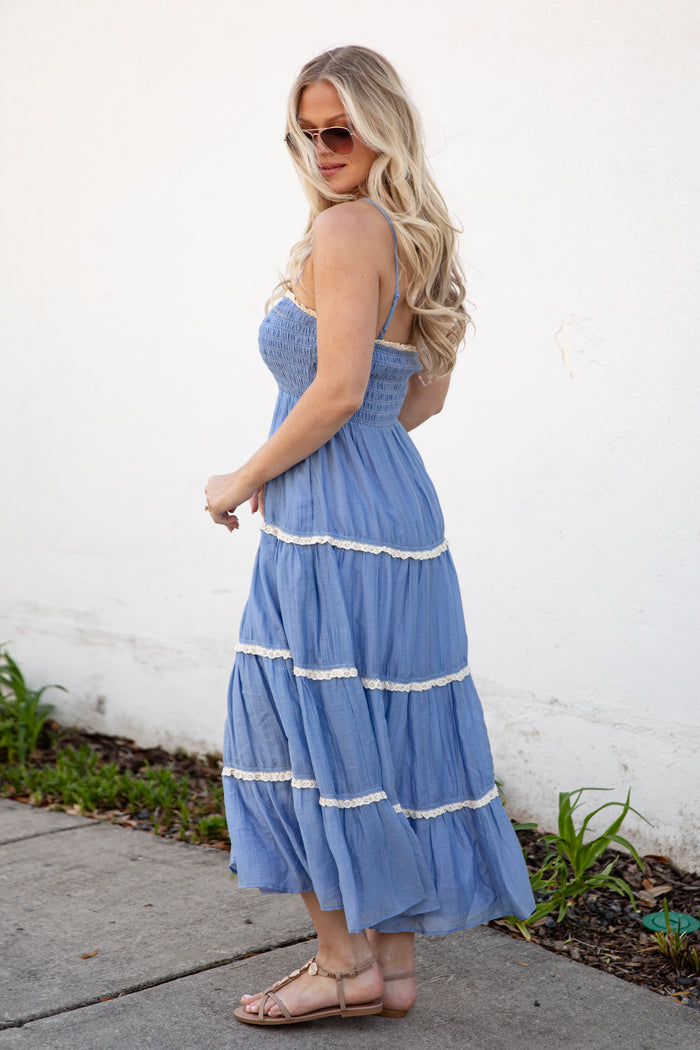 Woman wearing a blue dress with white trim standing against a white wall.