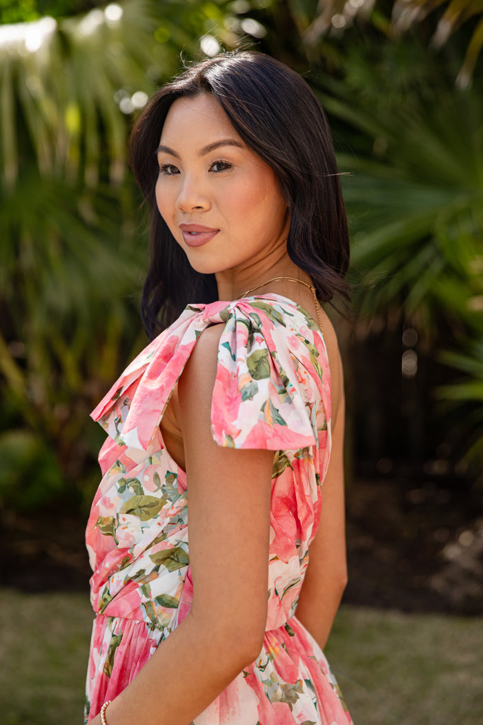 Woman wearing a pink floral dress standing in front of green foliage