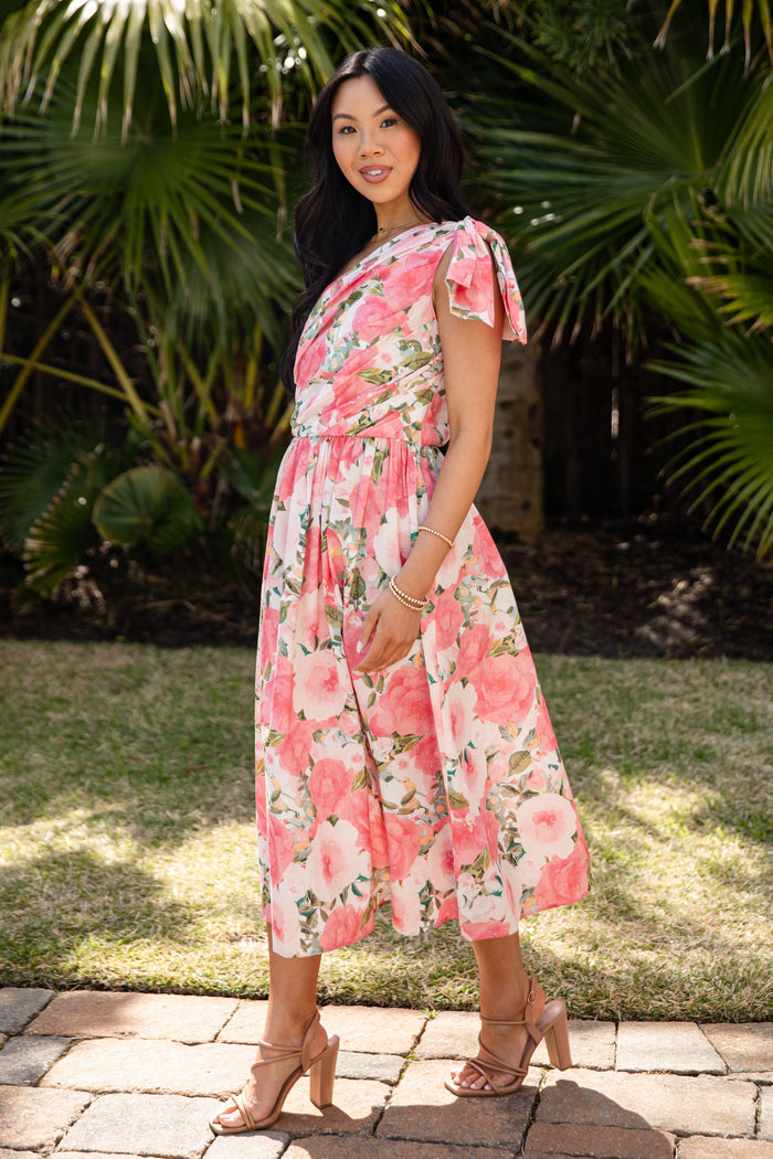 Woman wearing a floral dress standing outdoors with greenery in the background