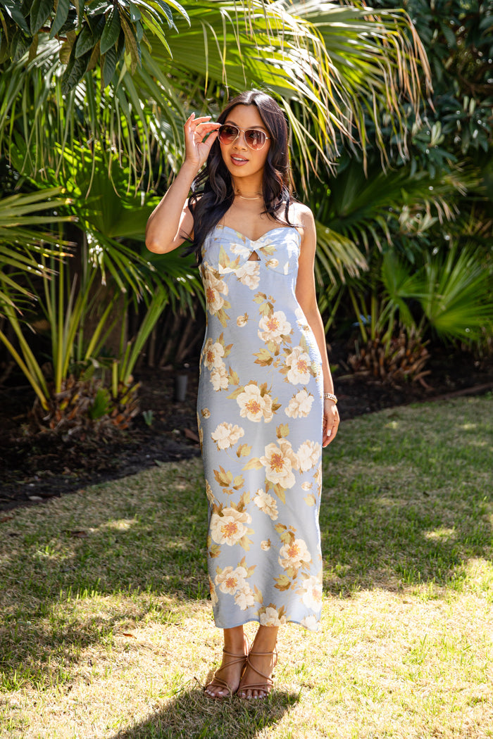 Woman in a floral dress standing outdoors with greenery in the background