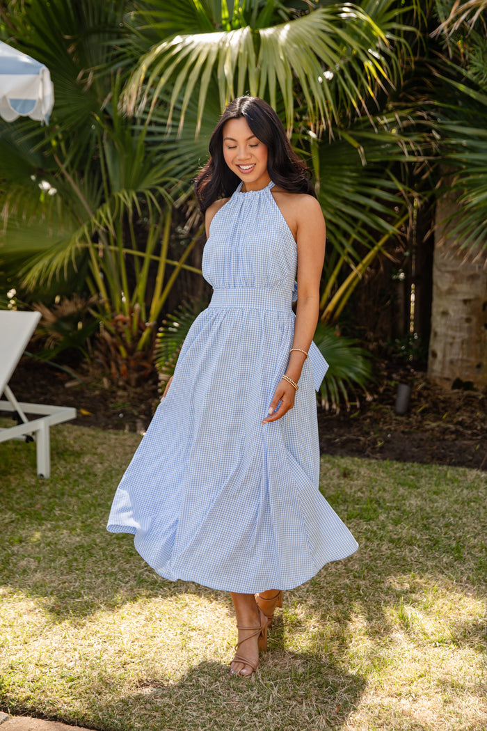Woman in a light blue dress standing outdoors with palm trees in the background