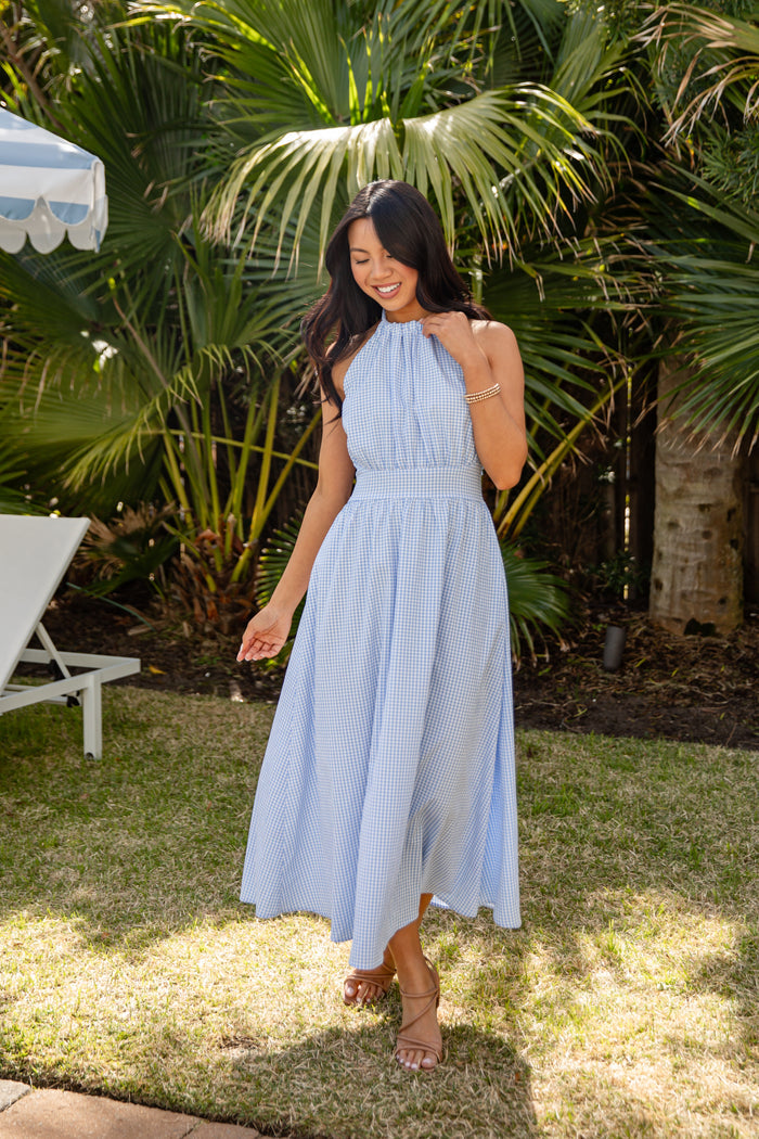 Woman in a light blue dress standing in a garden with palm trees.