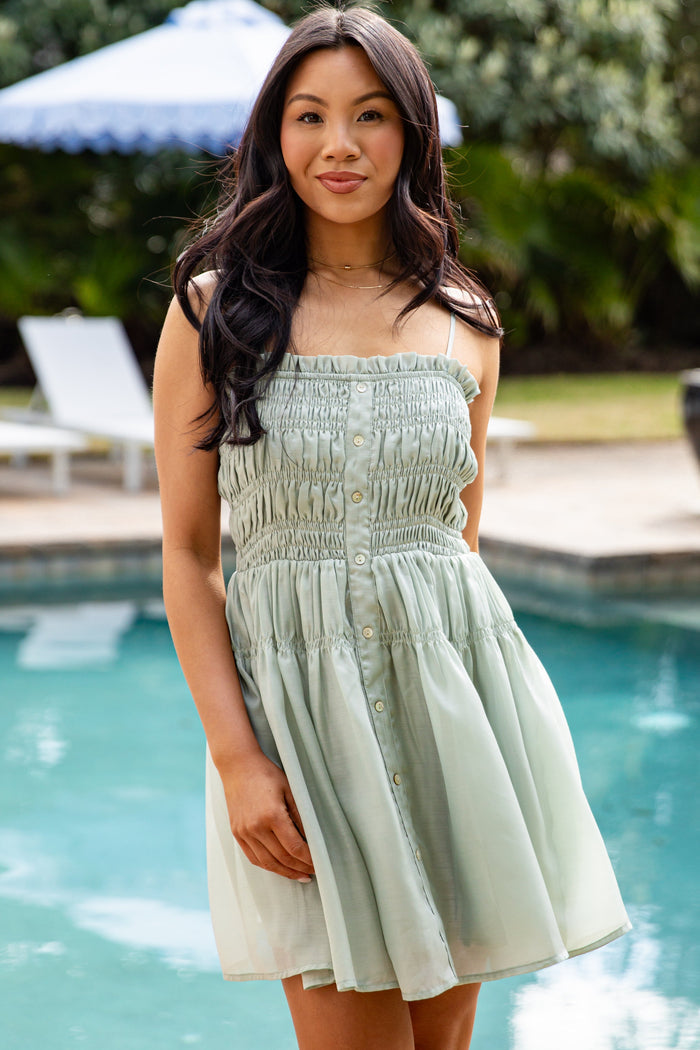 Woman in a light green dress standing by a pool with greenery in the background