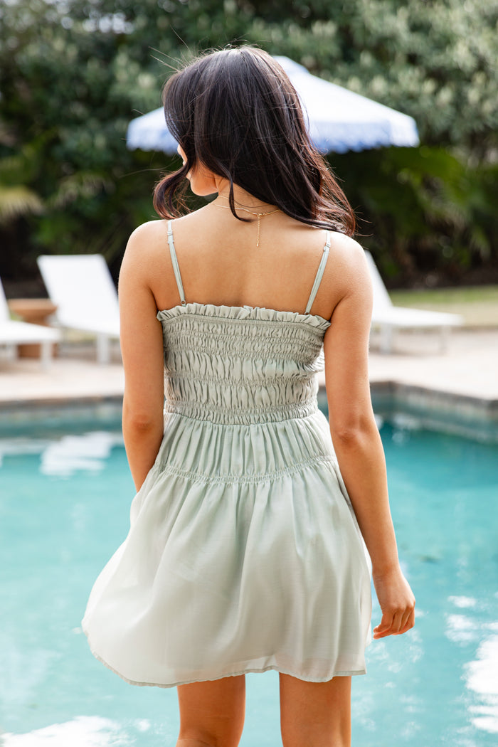 Woman in a light dress standing by a pool with greenery in the background
