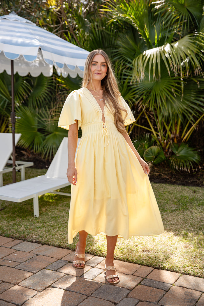 Woman in a yellow dress standing outdoors with palm trees in the background