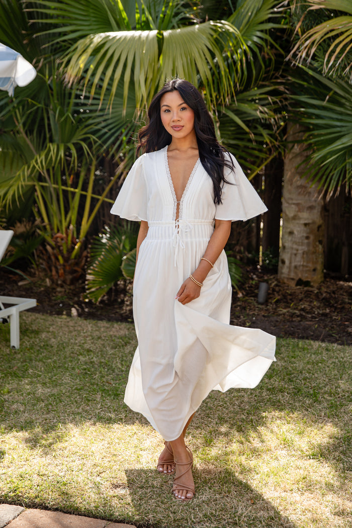 Woman in a white dress standing outdoors with greenery in the background