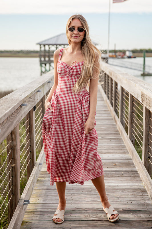 Woman in a red and white checkered dress standing on a wooden dock by a body of water.