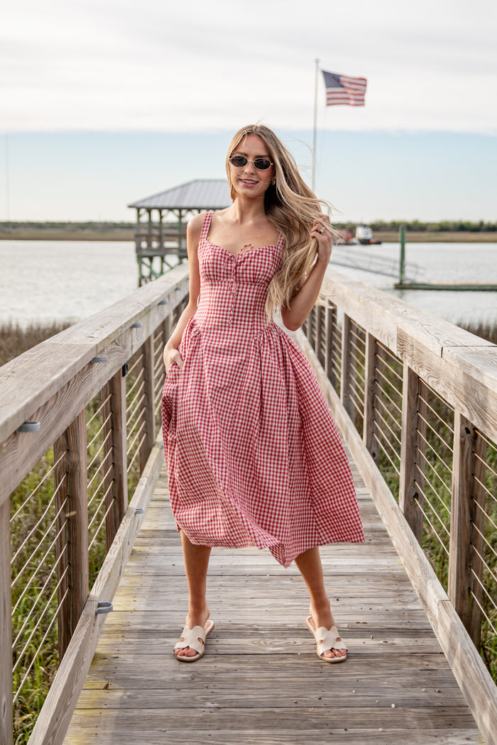 Woman in a red checkered dress standing on a wooden dock with an American flag in the background.
