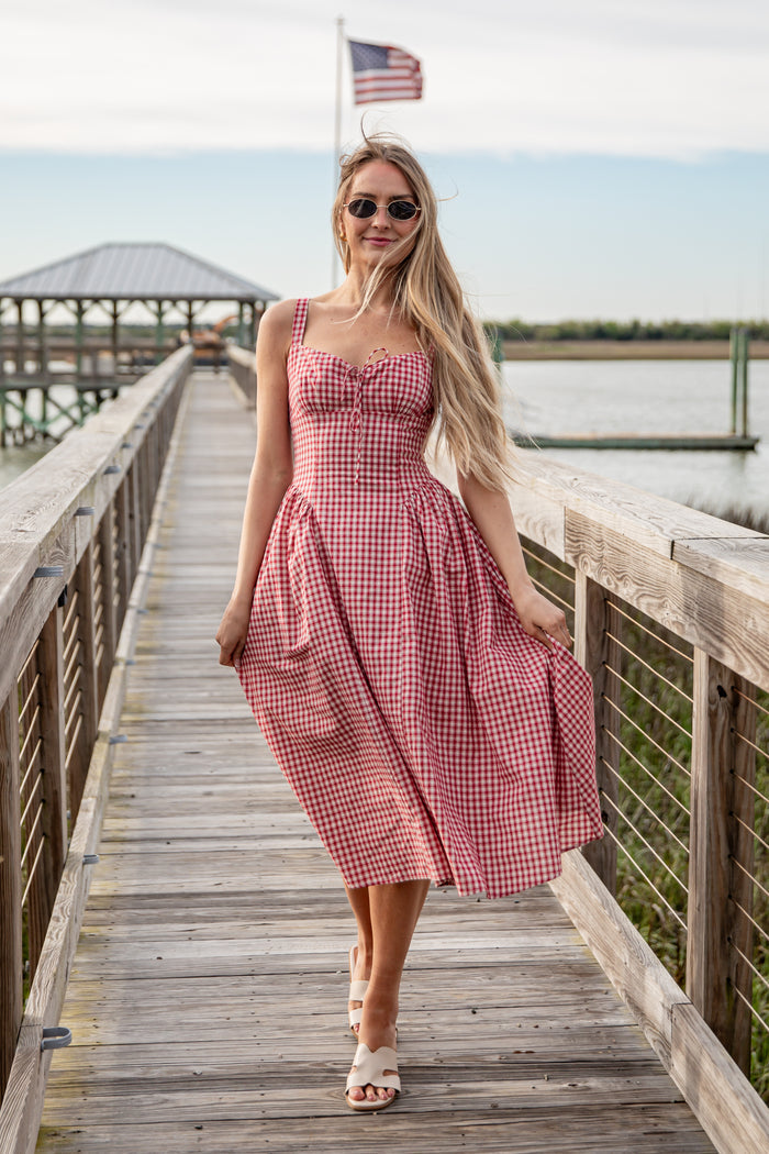Woman in a red checkered dress standing on a wooden dock with an American flag in the background.