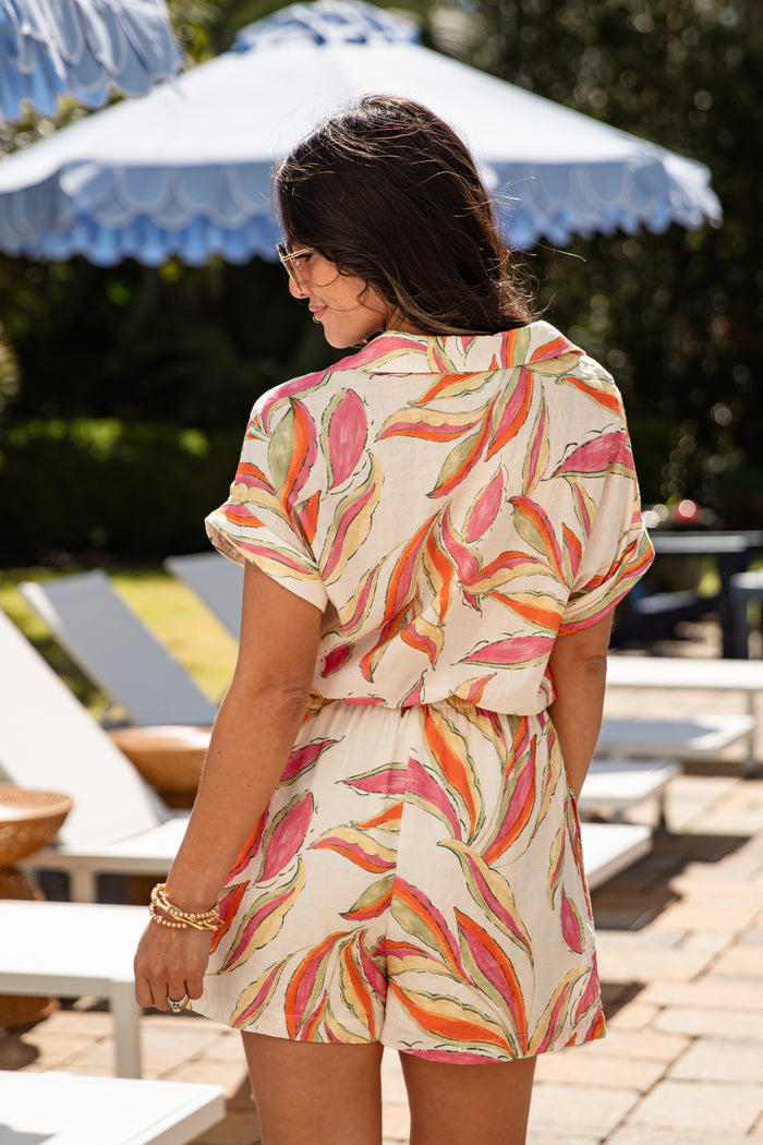 Woman wearing a colorful floral dress in an outdoor setting with lounge chairs and umbrellas.
