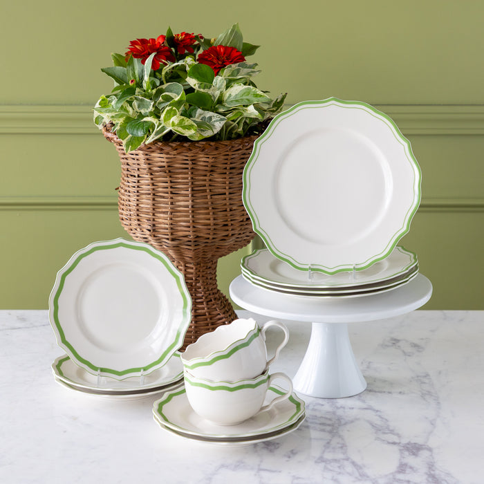 White ceramic plates with green rims on a marble surface, with a plant in the background.