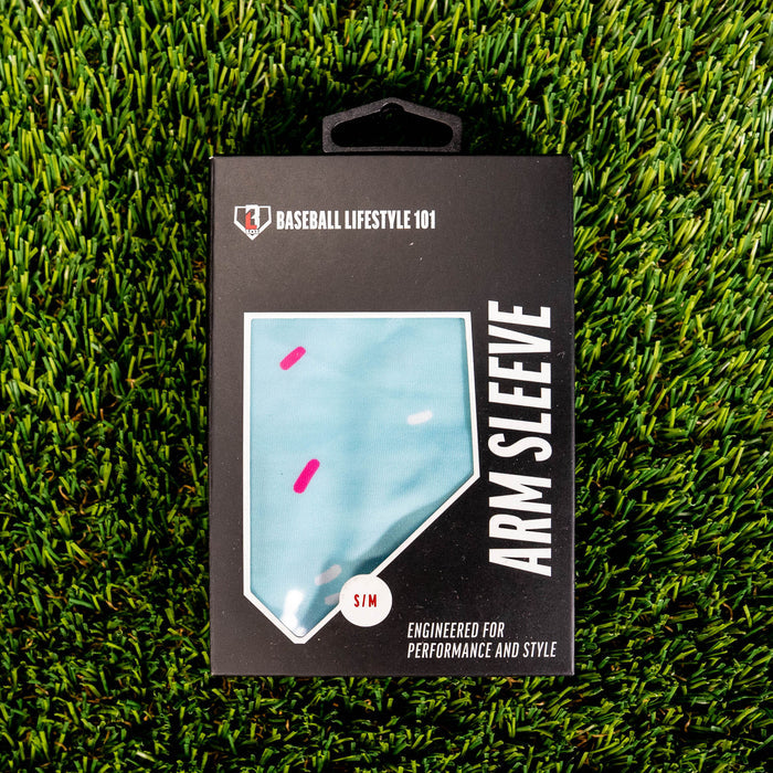 Front of the BL101 arm sleeve retail box on green turf showing the light blue sprinkle print through a home plate window and S/M size label