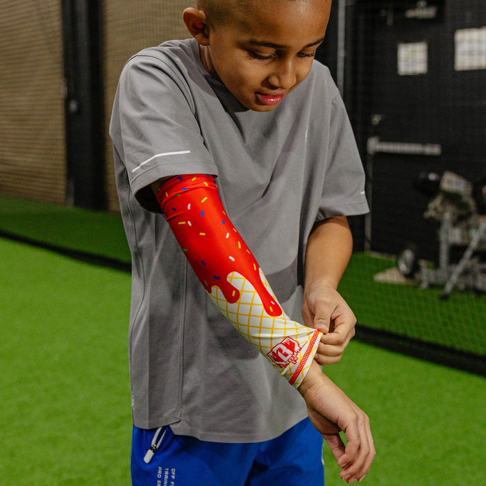 Young baseball player in a gray shirt pulling down the ice cream arm sleeve at the wrist in an indoor facility