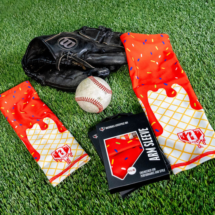Two ice cream arm sleeves laid on green turf next to a baseball a glove and the BL101 retail box showing the red sprinkle and waffle cone print