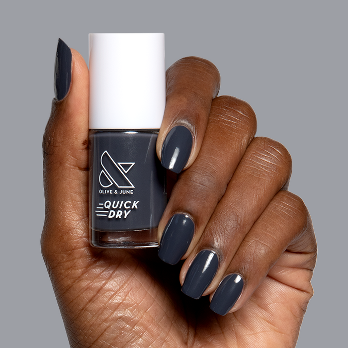 Hand with smooth nails painted in Inkling gel polish holding quick dry bottle against neutral background