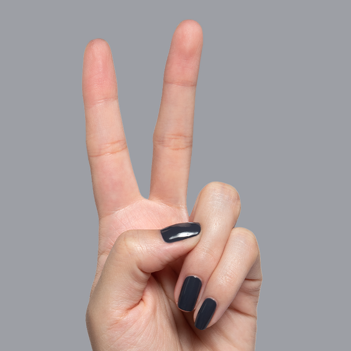 Hand with short nails painted in glossy Inkling gel polish showing a sleek quick dry mani on gray background